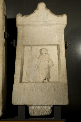 figura maschile stante in posizione frontale e (a sinistra) un bastone con avvolto un serpente (rilievo, stele a frontone con rilievo funerario e iscrizione, a Sosos) - Ambito culturale greco (prima metà sec. II a.C.)